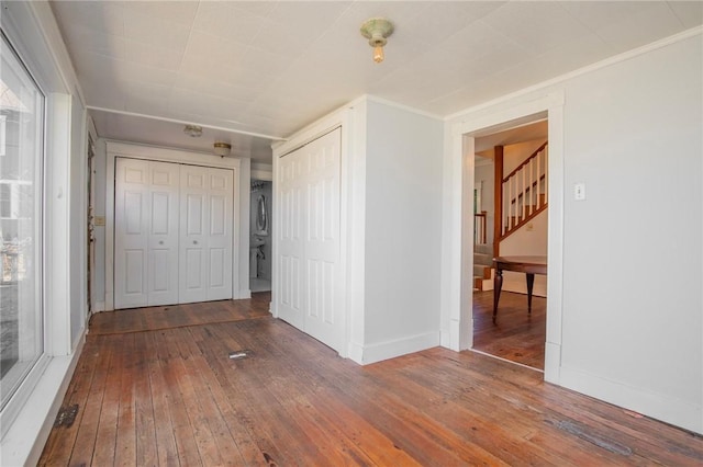 unfurnished bedroom with stacked washer / dryer, baseboards, and wood-type flooring