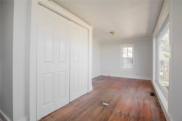 unfurnished bedroom with dark wood finished floors, visible vents, crown molding, and a closet