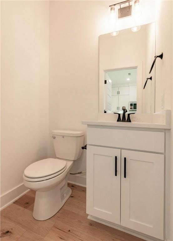 half bath featuring baseboards, toilet, wood finished floors, and vanity