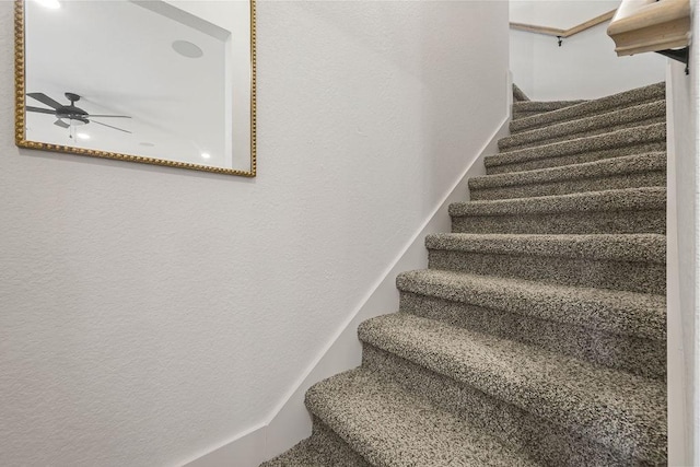 stairs featuring a ceiling fan