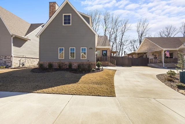 view of side of property featuring concrete driveway, fence, brick siding, and a chimney