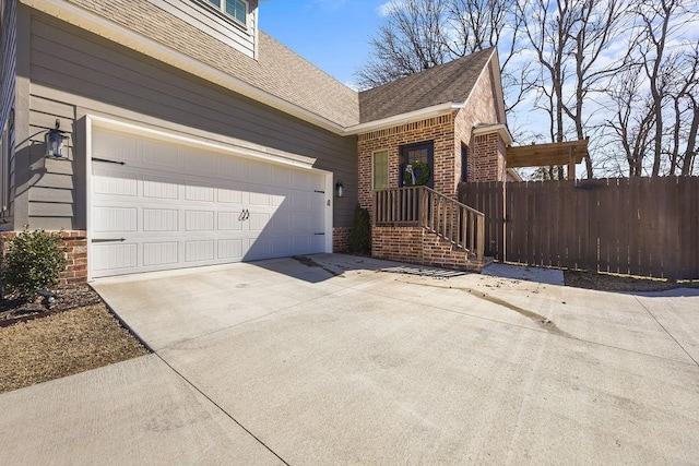 view of side of home featuring fence, roof with shingles, concrete driveway, a garage, and brick siding