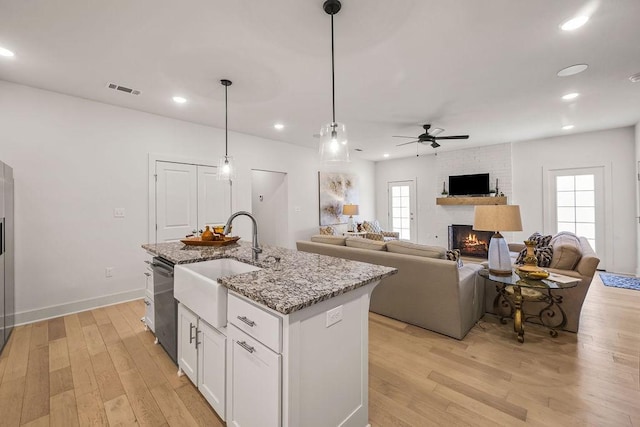 kitchen featuring a brick fireplace, visible vents, light wood finished floors, and a sink