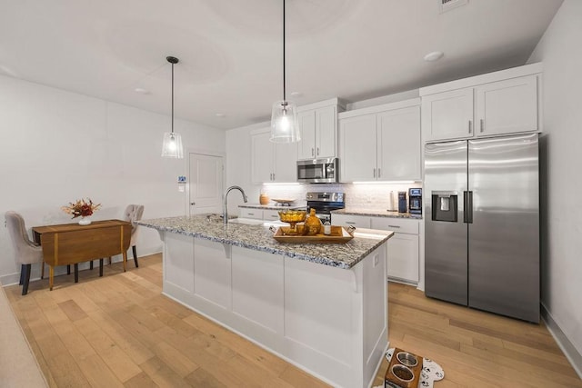 kitchen with light wood-style flooring, light stone counters, backsplash, stainless steel appliances, and white cabinets