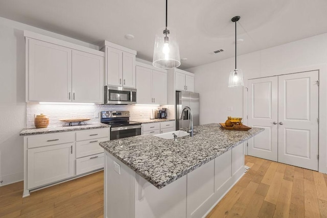 kitchen with white cabinets, stainless steel appliances, light wood-style flooring, and a sink