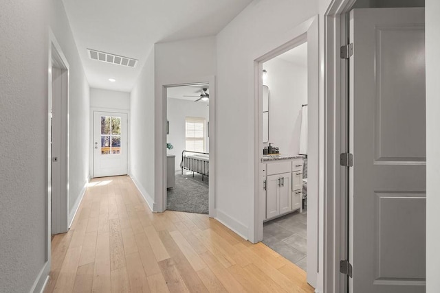 hallway with light wood-style floors, visible vents, and baseboards