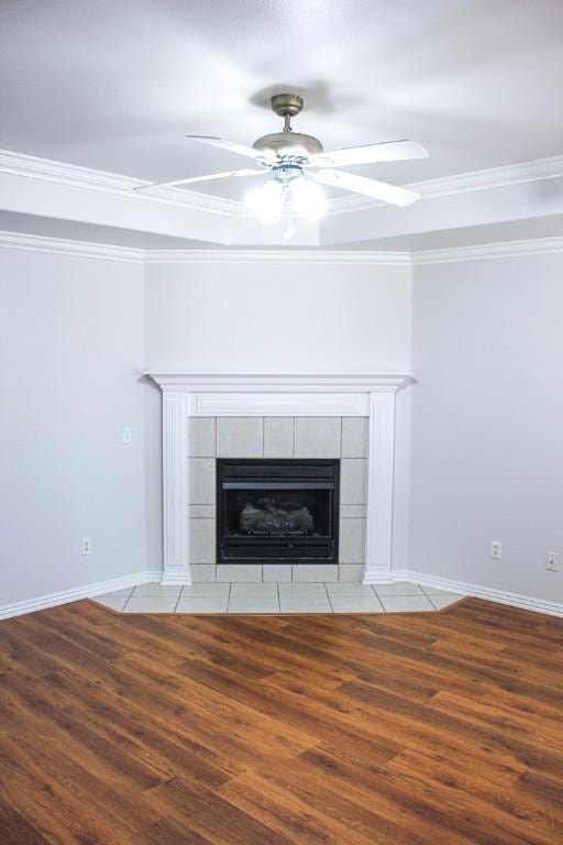 room details with crown molding, baseboards, ceiling fan, a tile fireplace, and wood finished floors