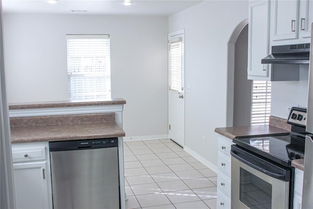 kitchen with dark countertops, under cabinet range hood, appliances with stainless steel finishes, arched walkways, and light tile patterned flooring