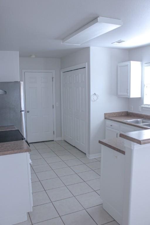 kitchen with a sink, freestanding refrigerator, white cabinets, light tile patterned floors, and baseboards