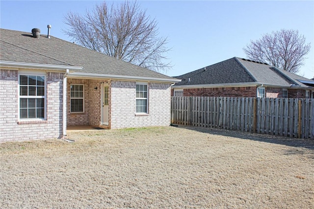 back of property featuring a lawn, fence, brick siding, and a shingled roof