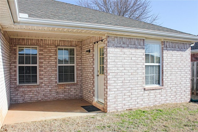 view of exterior entry featuring a patio, brick siding, and a shingled roof