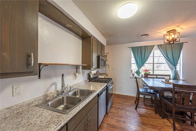 kitchen with a sink, a textured ceiling, dark wood finished floors, appliances with stainless steel finishes, and light countertops