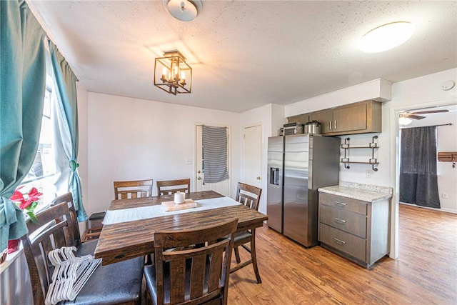 dining space featuring ceiling fan with notable chandelier, light wood finished floors, and a textured ceiling