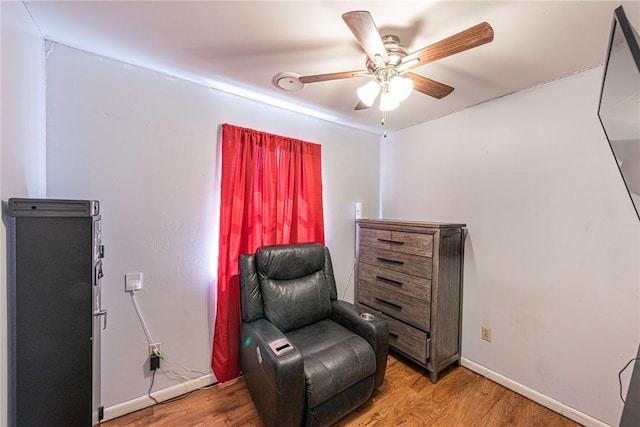 living area featuring light wood-style flooring, a ceiling fan, and baseboards