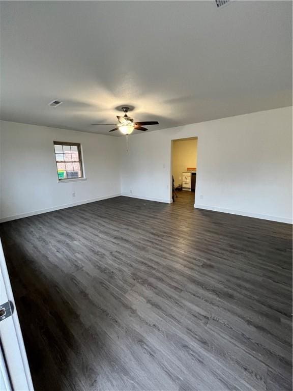 spare room with visible vents, a ceiling fan, dark wood-style flooring, and baseboards