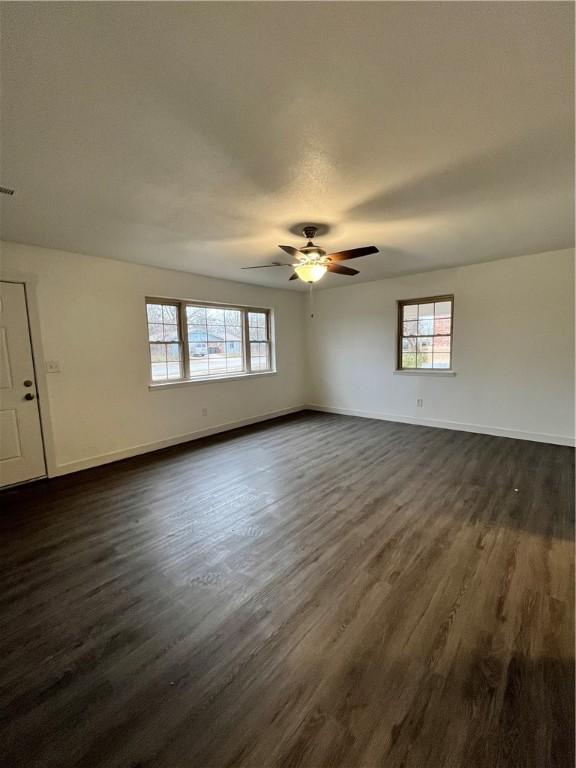 empty room with dark wood finished floors, plenty of natural light, a ceiling fan, and baseboards