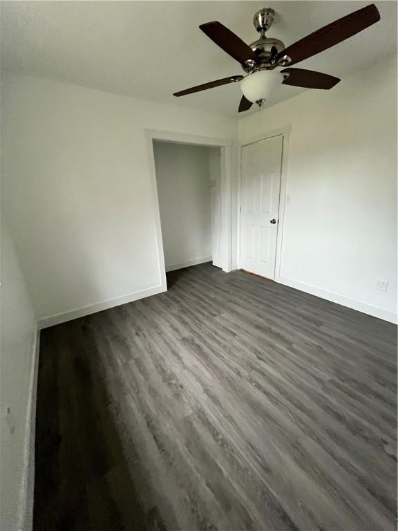 unfurnished bedroom with dark wood finished floors, a closet, baseboards, and a ceiling fan