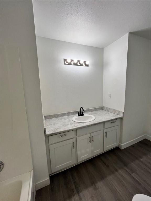 full bath featuring vanity, wood finished floors, baseboards, a bathing tub, and a textured ceiling