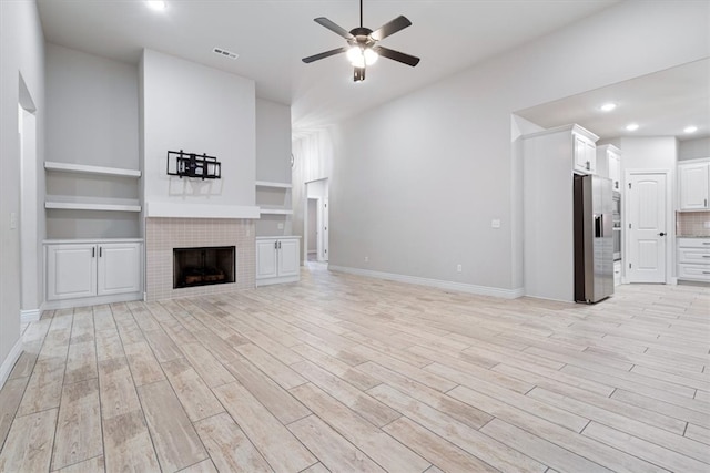 unfurnished living room featuring visible vents, light wood-style flooring, a ceiling fan, a tiled fireplace, and baseboards