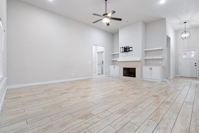 unfurnished living room with built in features, baseboards, a tiled fireplace, ceiling fan with notable chandelier, and light wood-type flooring