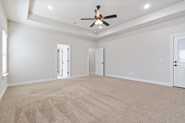 empty room featuring light carpet, visible vents, baseboards, and a tray ceiling