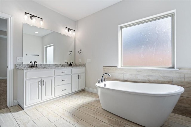 full bathroom with a sink, a freestanding bath, wood finished floors, and double vanity