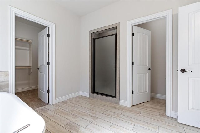 interior space featuring a shower stall, a freestanding bath, a walk in closet, and wood tiled floor