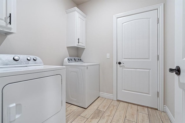 laundry area featuring wood finish floors, baseboards, cabinet space, and separate washer and dryer