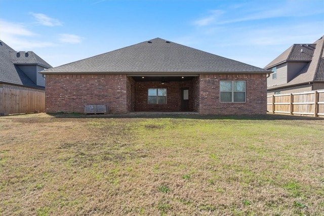 back of house featuring a lawn, brick siding, a fenced backyard, and a shingled roof