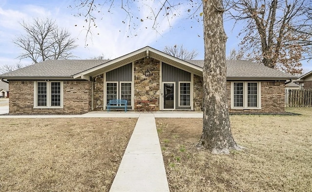 back of property featuring stone siding, fence, a yard, roof with shingles, and brick siding