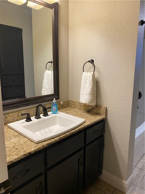 bathroom featuring vanity, tile patterned floors, a textured wall, and baseboards