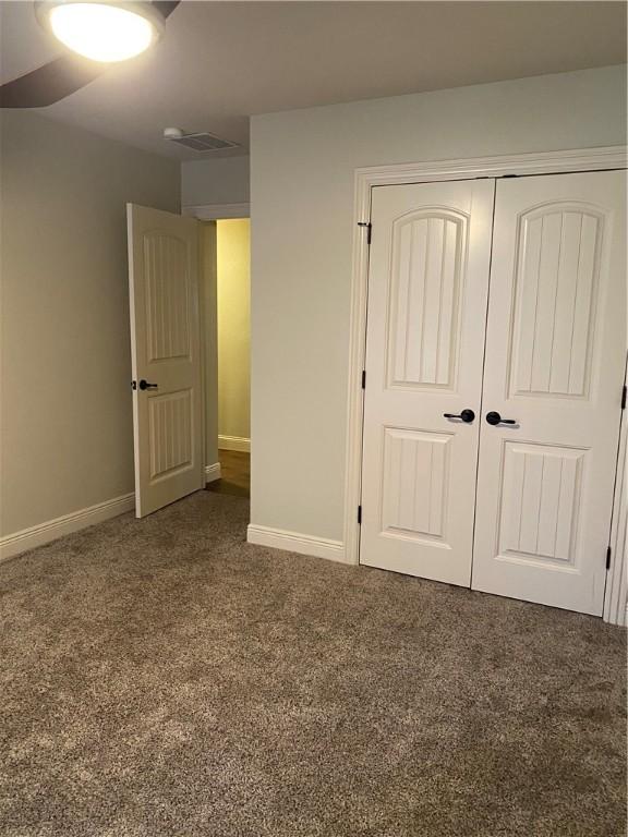 unfurnished bedroom featuring a closet, baseboards, visible vents, and dark carpet