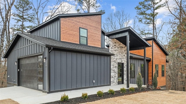 view of front of home featuring driveway, a shingled roof, a garage, stone siding, and board and batten siding