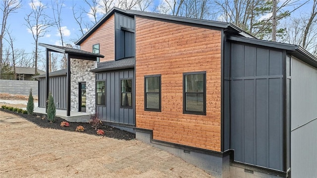 view of property exterior featuring crawl space, stone siding, board and batten siding, and fence