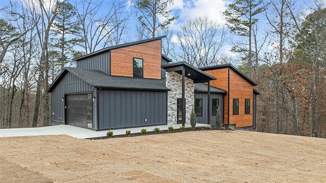 contemporary house featuring stone siding, board and batten siding, a shingled roof, and driveway