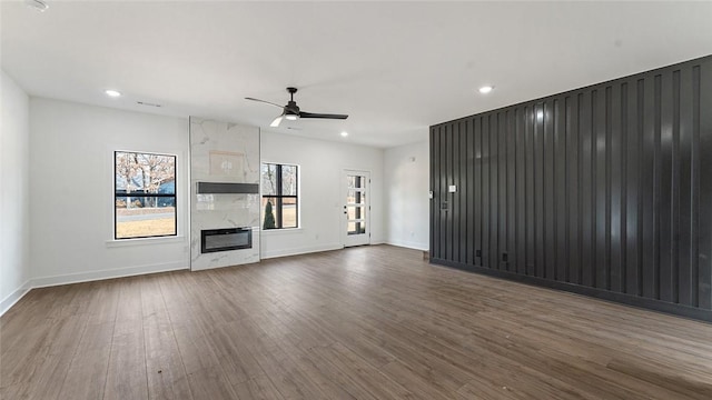 unfurnished living room featuring a premium fireplace, baseboards, ceiling fan, and dark wood-style flooring