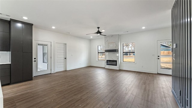 unfurnished living room featuring a high end fireplace, baseboards, dark wood finished floors, recessed lighting, and a ceiling fan