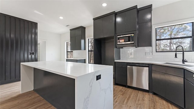 kitchen with light wood-style flooring, a sink, stainless steel appliances, light countertops, and backsplash