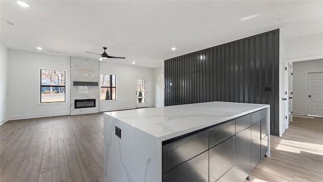 kitchen with ceiling fan, light wood-style flooring, a high end fireplace, and a center island