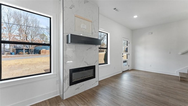 unfurnished living room with a wealth of natural light, visible vents, wood finished floors, and a premium fireplace