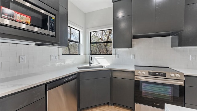 kitchen featuring light wood finished floors, backsplash, gray cabinetry, stainless steel appliances, and a sink