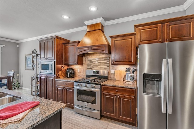 kitchen featuring light stone counters, custom range hood, appliances with stainless steel finishes, crown molding, and tasteful backsplash