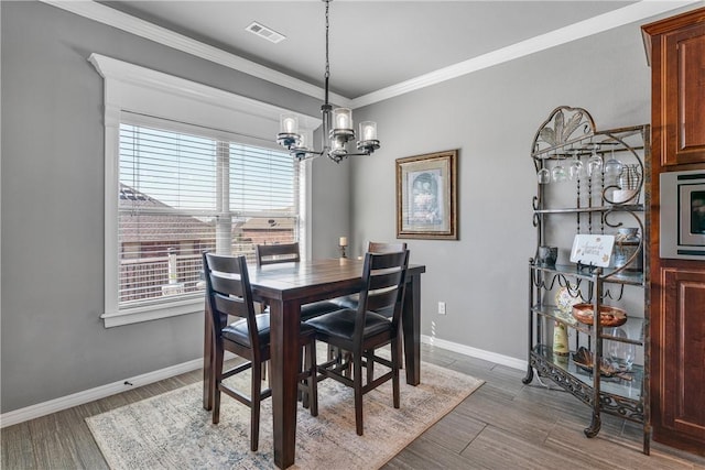 dining area with visible vents, wood finished floors, an inviting chandelier, and ornamental molding