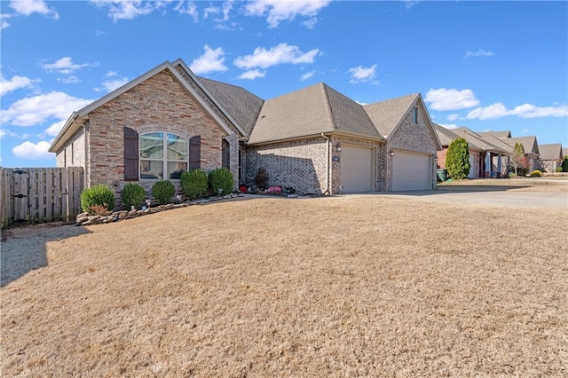 view of front of house with brick siding, a shingled roof, fence, driveway, and an attached garage