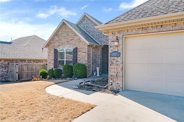 view of front of home featuring fence, a shingled roof, concrete driveway, a garage, and brick siding