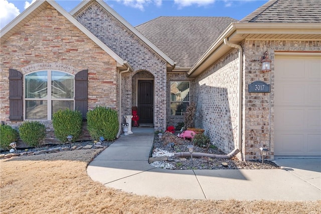 property entrance with brick siding, an attached garage, and a shingled roof