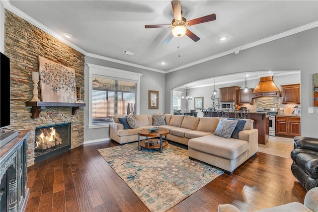 living room featuring visible vents, ceiling fan with notable chandelier, hardwood / wood-style floors, a fireplace, and crown molding