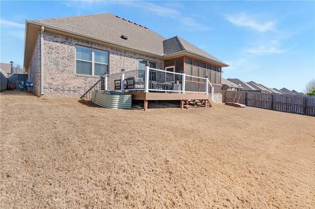 back of property with a wooden deck, a shingled roof, a fenced backyard, and brick siding