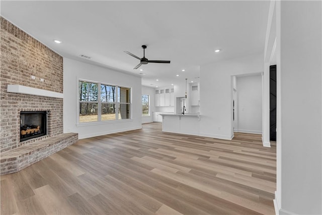 unfurnished living room featuring baseboards, light wood-style floors, ceiling fan, and a fireplace