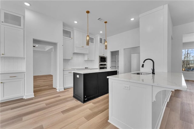 kitchen featuring a kitchen island with sink, a sink, appliances with stainless steel finishes, white cabinets, and decorative backsplash